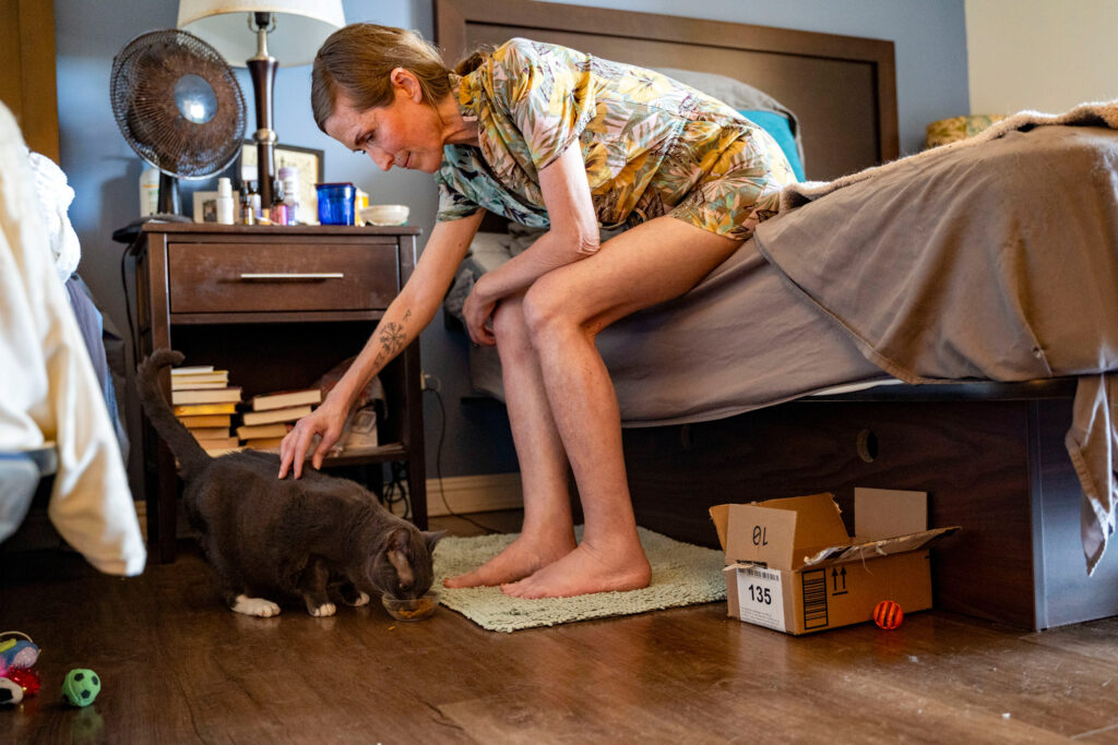 Mari Younger pets her cat Stella inside her converted hotel room where she lives after being displaced two years prior by the Maui fires, in Kihei, Hawaii, Wednesday, March 4, 2026. (AP Photo/Mengshin Lin)