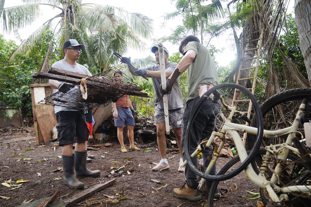 Les Romero, left, gets loaded up with debris by volunteers helping him clear his and his mother Loreta Romero’s  Kukea Loop home Sunday, March 22, 2026, in Waialua. A second Kona low storm brought heavy rain after the previous week’s downpour and high winds. Her son Les Romero’s phone number is 808-772-0313. (Kevin Fujii/Civil Beat/2026)