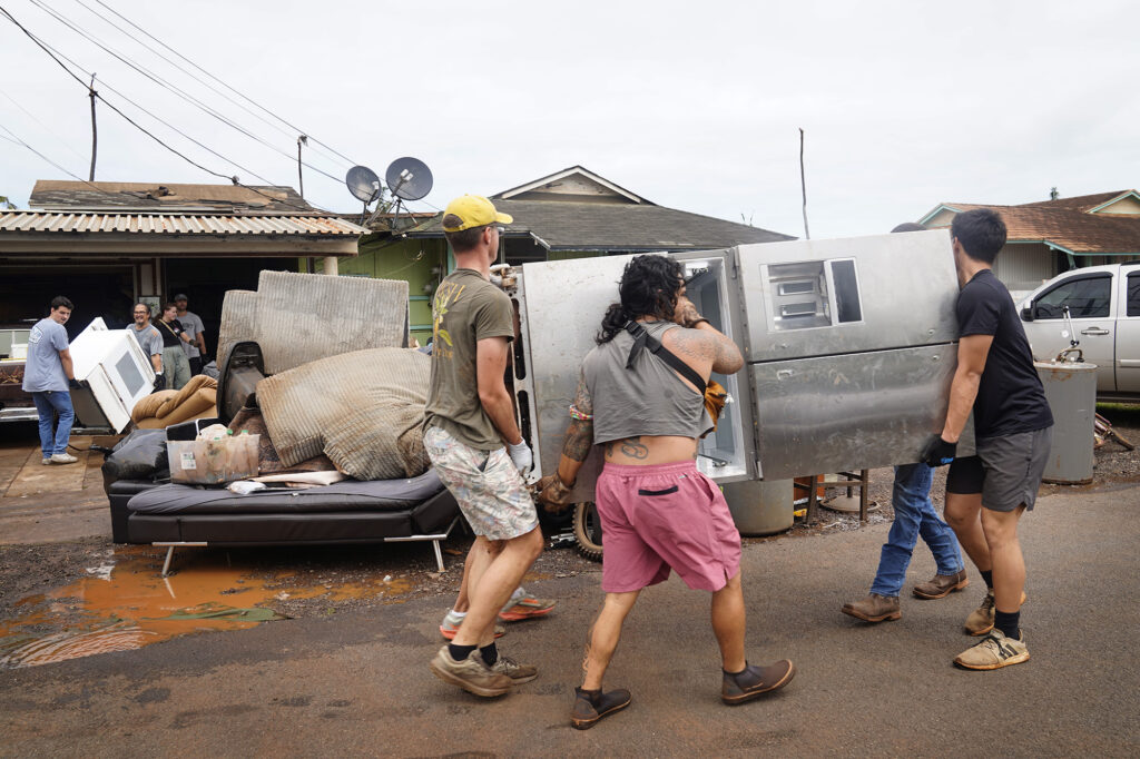 Volunteers carry out appliances from Sharmaine Arial’s Kukea Loop home Sunday, March 22, 2026, in Waialua. Sharmaine’s number is 808-970-4295. (Kevin Fujii/Civil Beat/2026)
