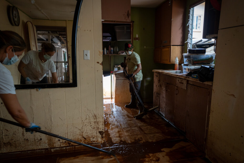 Nicole Fernandez, left, is reflected in a mirror as she and Vanessa Vizcarra volunterred to clean up Estrelita Andres' house on Waialua Beach Road March 24, 2026. Like the majority of volunteers, the two did not know the home owner. Heavy rainfall the last two weeks caused devastating flooding to area residents. (Craig Fujii/Civil Beat/2026)