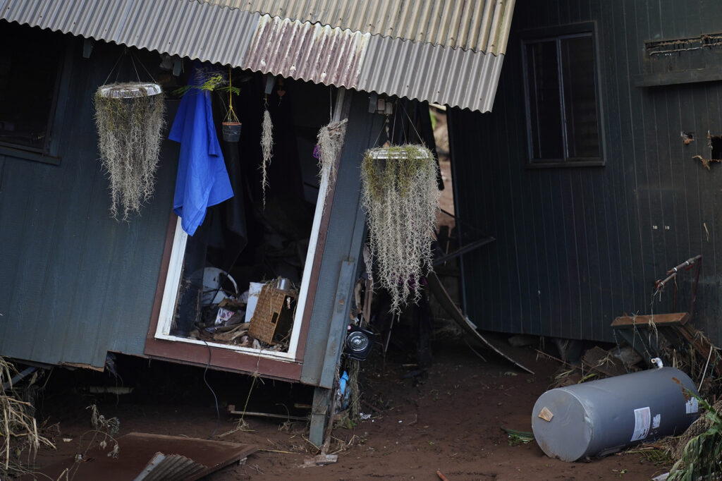 Hanging plants show the correct vertical orientation compared to askew Otake Camp homes which were dislodged from their foundations during a Kona Low storm flood Wednesday, March 25, 2026, in Waialua. The former plantation residential neighborhood received damage from the second Kona Low storm. (Kevin Fujii/Civil Beat/2026)