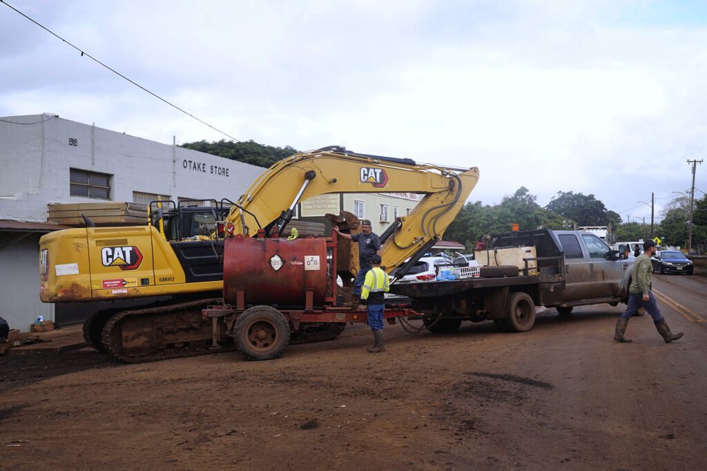 Privately donated diesel fuel tops off a privately owned hydraulic crawler excavator to work on cleaning up Otake Camp Wednesday, March 25, 2026, in Waialua. The former plantation residential neighborhood received damage from the second Kona Low storm. (Kevin Fujii/Civil Beat/2026)
