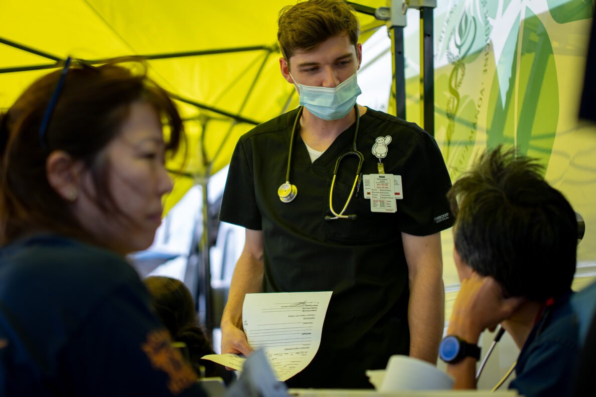Student doctor Lincoln Hunt, center, presents his case to attending physician Yusuke Kobayashi, right, at a mobile clinic at Ali'i Beach Park in Haleiwa March 26, 2026. Physician Tracie Hata is at left. Students at John A. Burns School of Medicine (JABSOM) staffed the clinics to aid local residents affected by flooding in Haleiwa and Waialua. (Craig Fujii/Civil Beat/2026)