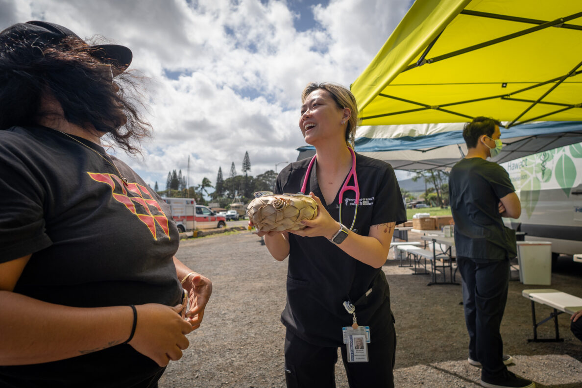 Student doctor Tracie Okumura, receives a woven bowl of coffee cups from Andreanna Kaluhiokalani, left, as she and other students from John A. Burns School of Medicine provided on-site care to local residents at Ali'i Beach Park in flood-ravaged Haleiwa March 26, 2026. Kaluhiokalani's family owns the coffee shop, Love Like Buttons. (Craig Fujii/Civil Beat/2026)