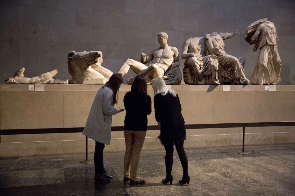 FILE - Women stand by a marble statue of a naked youth thought to represent Greek god Dionysos, center, from the east pediment of the Parthenon, on display during a media photo opportunity to promote a forthcoming exhibition on the human body in ancient Greek art at the British Museum in London, on Jan. 8, 2015. The chairman of the British Museum said Thursday, Feb. 16, 2023 the U.K. and Greece are working on a deal that would see the Parthenon Marbles displayed in both London and Athens. The antiquities, also known as the Elgin Marbles, are the remnants of a frieze that ran around the outer walls of the Parthenon temple on the Acropolis in Athens. (AP Photo/Matt Dunham, File)