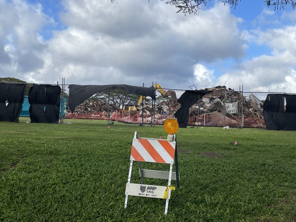 Black screens hanging on a barrier fence that surrounds tons of flood debris from the March 20206 storms on Oahu.