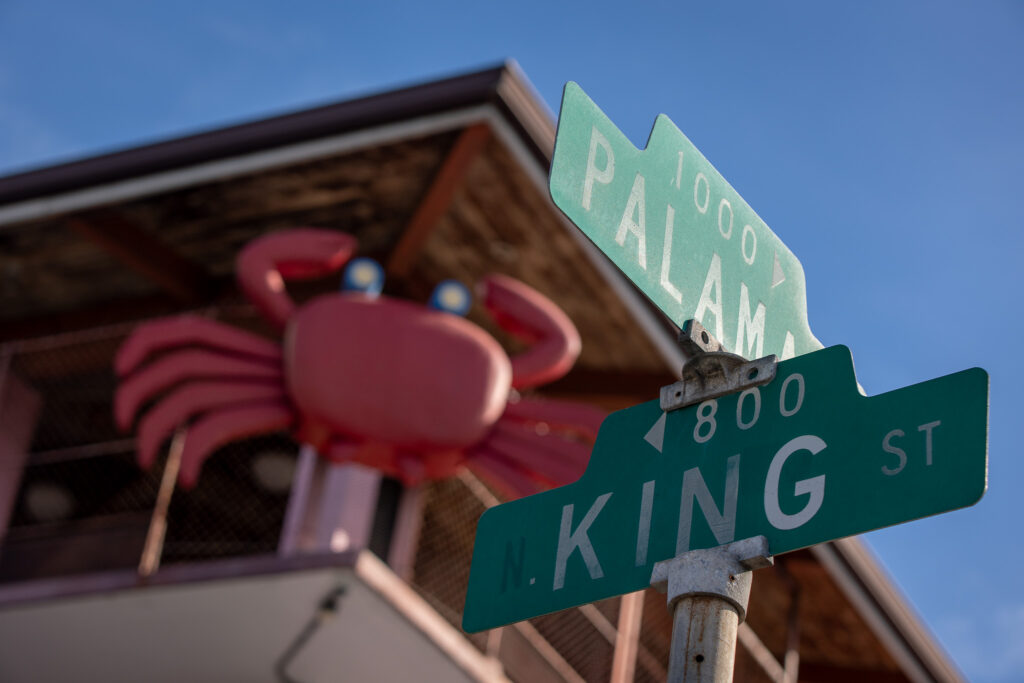 Green street signs mark the site of a pink building with a large decorative crab.