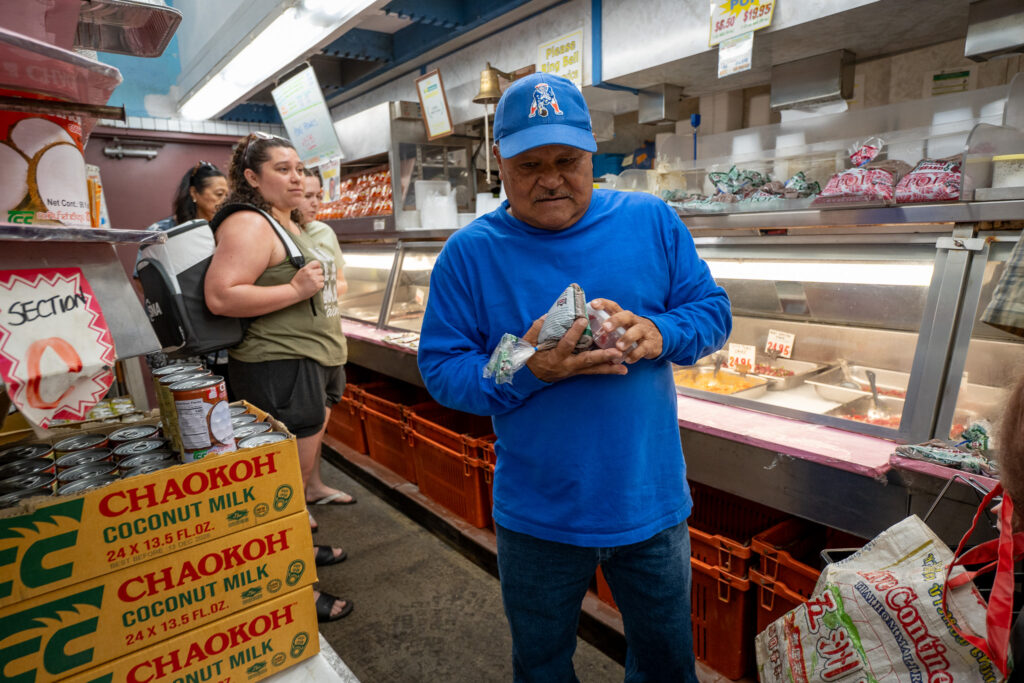 Longtime customer Gye Kaneshiro, 64, (cq, pronounced "Guy") grabs poi and half pound of poke or breakfast at Tamashiro Market April 3, 2026. The market, which opened in 1941, closes April 30th. (Craig Fujii/Civil Beat/2026)