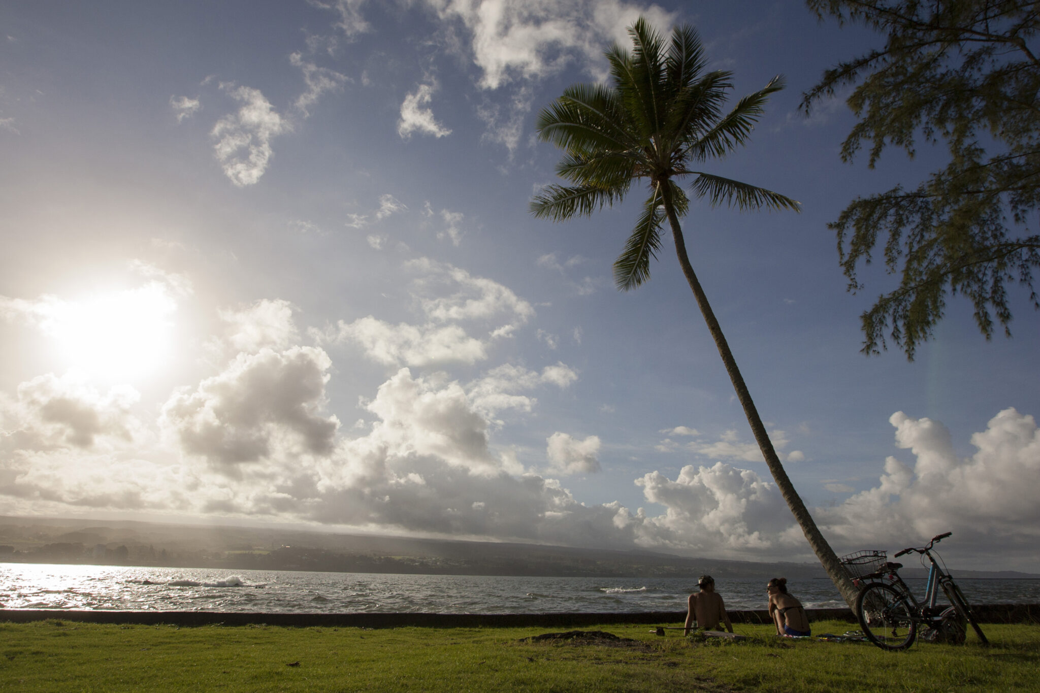 FILE - In this Aug. 30, 2015, file photo, Keenin Ide, left, of Hilo, Hawaii, and Medea Yankova, of Sofia, Bulgaria, sit near Hilo Bay in Hilo, Hawaii. The Big Island visitors bureau and Hawaii County have launched a campaign that aims to create a more conscientious tourism industry on the Big Island. The Island of Hawaii Visitors Bureau Executive Director Ross Birch and county Managing Director Will Okabe presented the new "Pono Pledge" at a Thursday, Sept. 20, 2018, event, the Hawaii Tribune-Herald reported.  (AP Photo/Caleb Jones, File)
