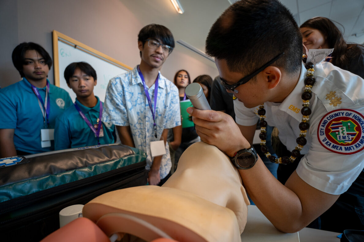 EMT Cameron Hara shows students how to place a breathing tube in an airway mannequin during an education event at JABSOM April 7, 2026. From left, Jayden Cabel-Suehiro, Jaiden Aquino and Zander Munalem look on.