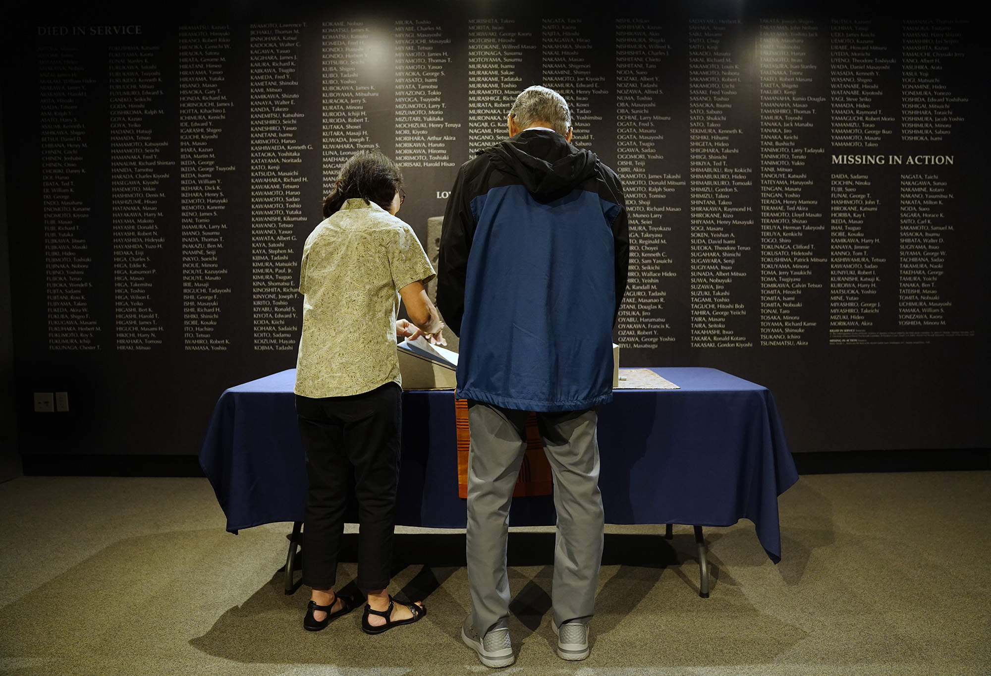 My father Kazuo Fujii watches an Ireichō staffer turn pages containing 125,284 names of those of Japanese ancestry imprisoned in War Relocation camps and assembly center detention facilities during World War II in front of a wall with names of Nisei soldiers killed or missing in action Thursday, April 9, 2026. (Kevin Fujii/Civil Beat/2026)