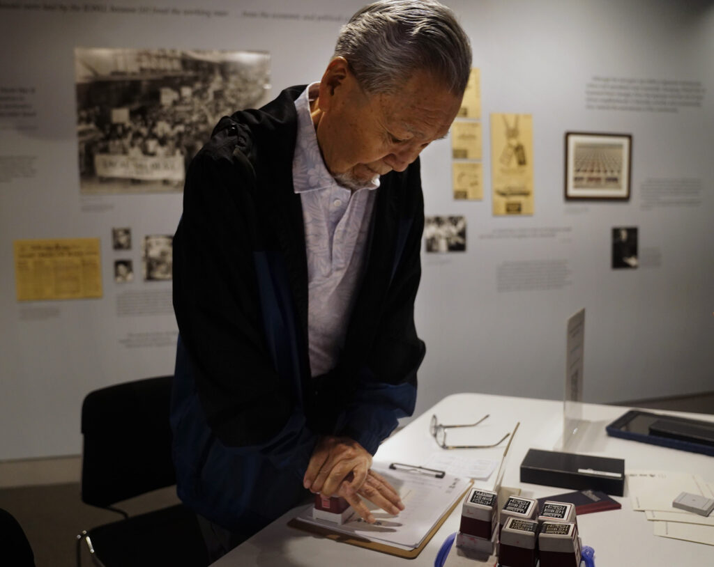 Kazuo Fujii puts his weight into a commemorative stamp after placing a Japanese hanko (stamp) on his and his relatives names in the Ireichō Thursday, April 9, 2026, in Honolulu. (Kevin Fujii/Civil Beat/2026)