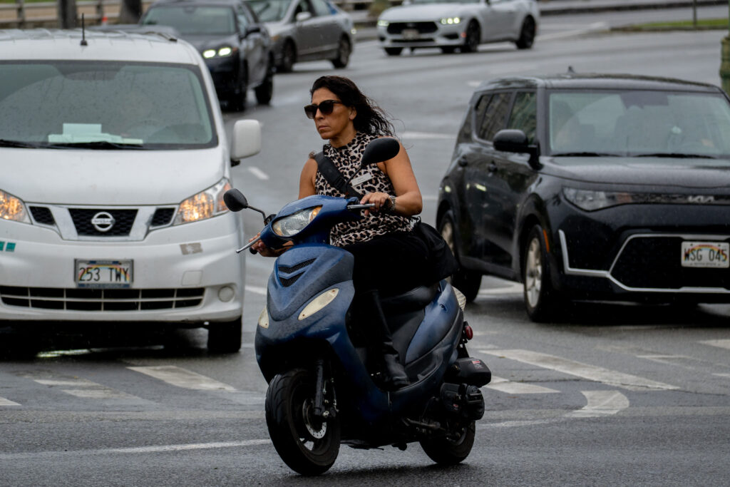 An unhelmeted moped rider on Kalakaua Avenue in Waikiki April 13, 2026. (Craig Fujii/Civil Beat/2026)