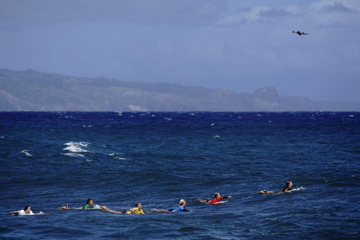 The inaugural Hawaiʻi High School Athletics Association surfing championships girls shortboard semifinal paddles toward the set of incoming waves as a drone flies overhead Saturday, May 2, 2026, at Hoʻokipa Beach Park in Pāʻia. (Kevin Fujii/Civil Beat/2026)