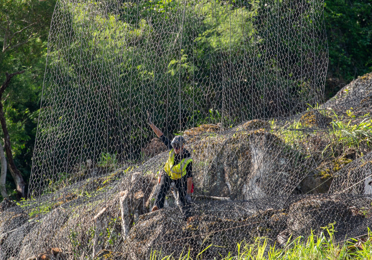 A worker guides rockfall safety netting onto an unstable hill above Waimea Bay May 17, 2026. Boulders fell onto the roadway in early April which kickstarted stabilization work. (Craig Fujii/Civil Beat/2026)