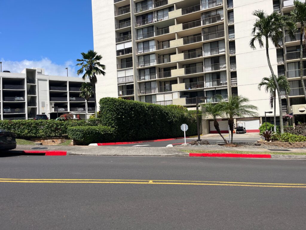 Red painted stripes on roadside curbs in the middle ground with a street in front of the curb and an apartment building in the background.