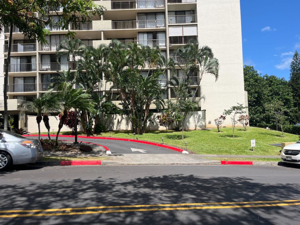 Red paint on a curb in the middle ground with a street in the foreground and an apartment block in the background.