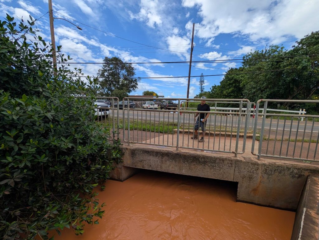 Kanoa Dahlin stands on a culvert many have blamed for being too small, too clogged and too overwhelmed to handle the floodwaters coming from uphill during the March Kona low storms.
