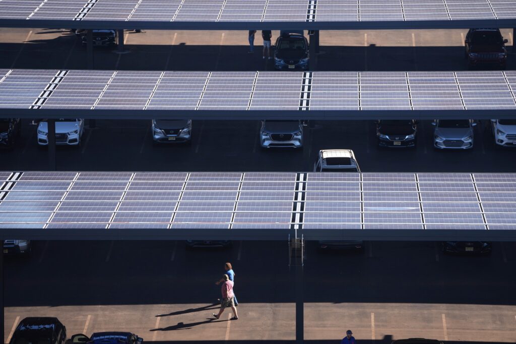 FILE - People walk though a parking lot with solar panels near Lincoln Financial Field, Sept. 8, 2025, in Philadelphia. (AP Photo/Matt Slocum, File)