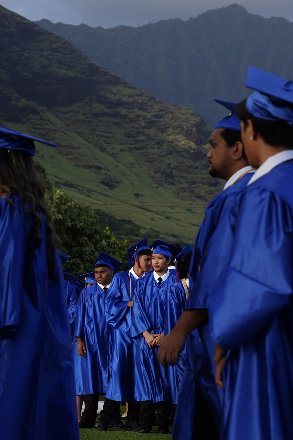 The Waiʻanae Mountain Range rises behind Waiʻanae High School seniors in cap and gown as they enter their commencement ceremony Friday, May 22, 2026, in Waiʻanae. (Kevin Fujii/Civil Beat/2026)