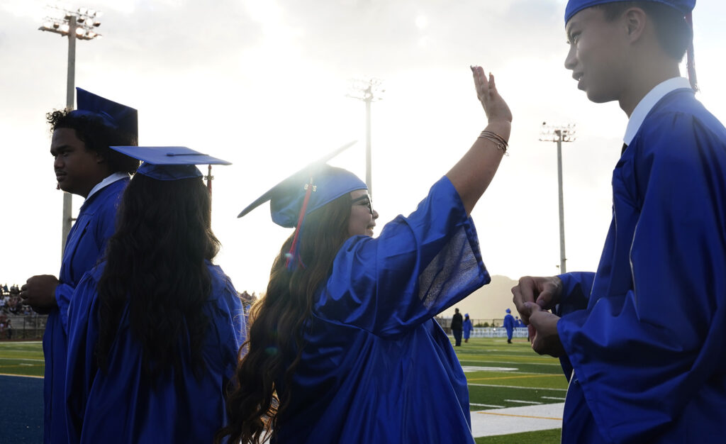 Waiʻanae High School senior Kawehi Windham waves to ʻohana and friends before the commencement ceremony Friday, May 22, 2026, in Waiʻanae. (Kevin Fujii/Civil Beat/2026)